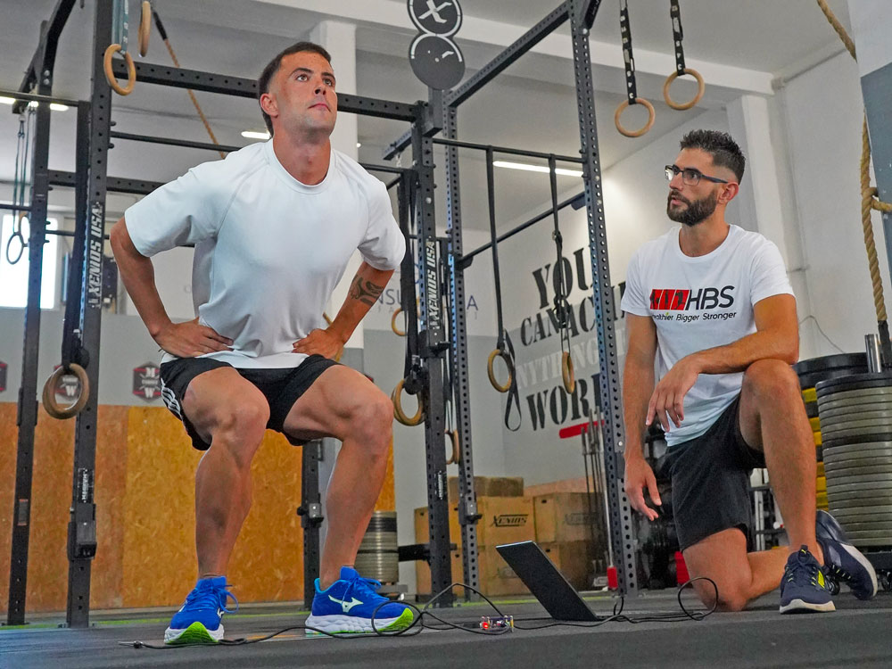 Uomo che esegue squat sotto la supervisione di un coach HBS per valutazione sportiva.