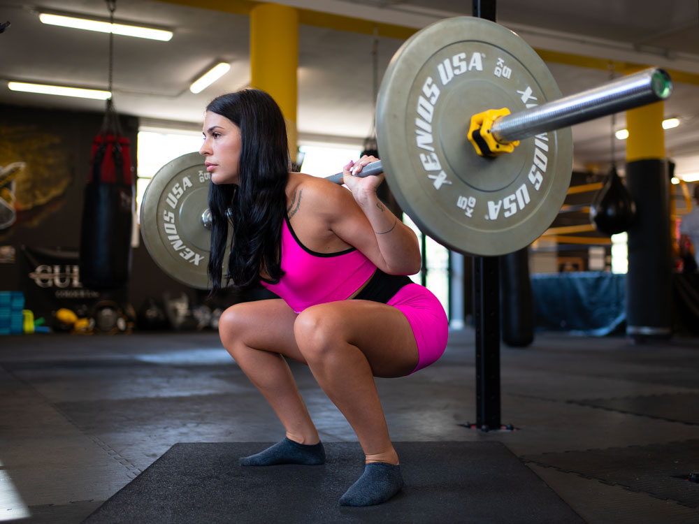 Atleta femminile esegue squat con bilanciere, allenamento di forza con Hbs Coaching.